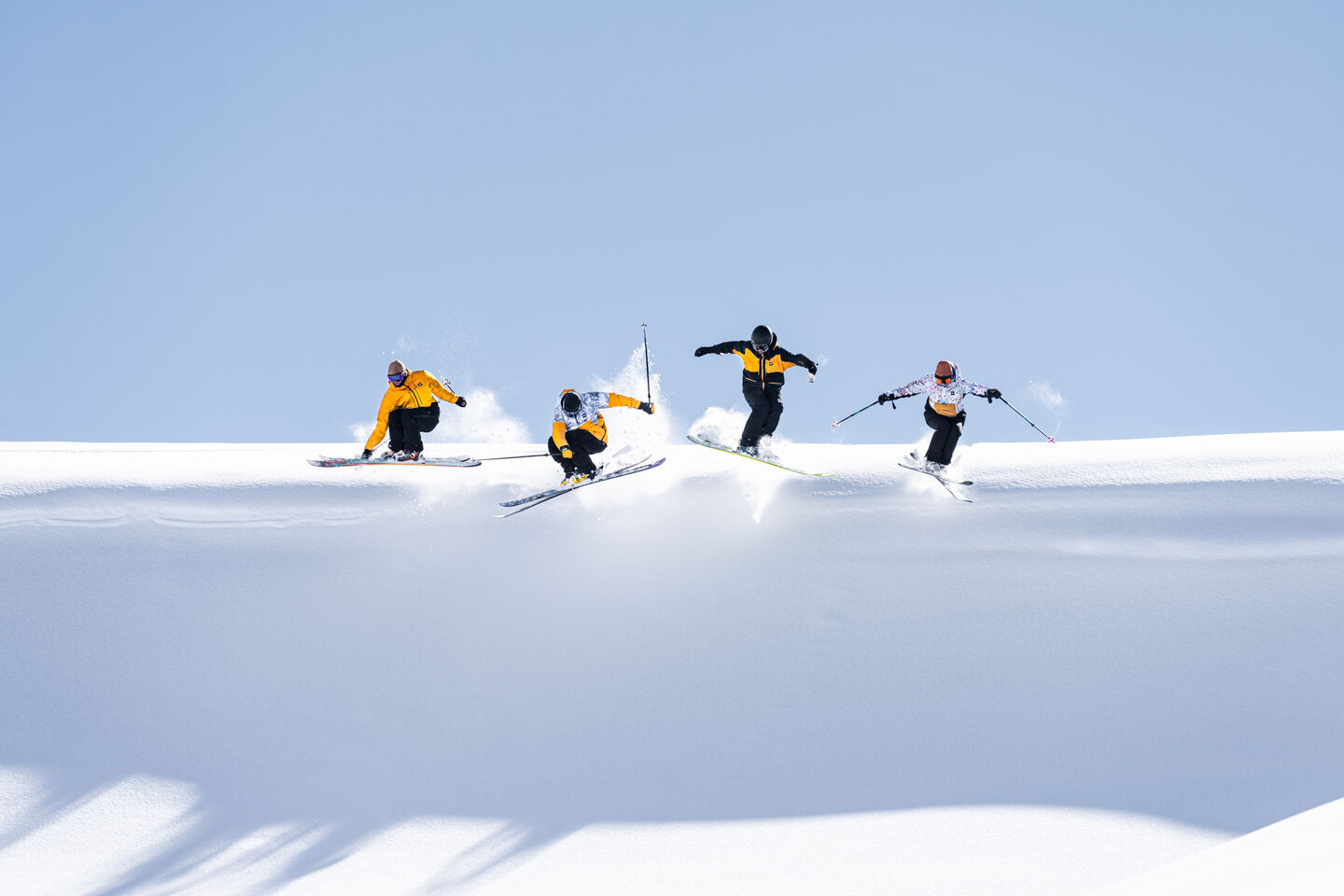four skiers in yellow jackets jumping off a hill at the same time